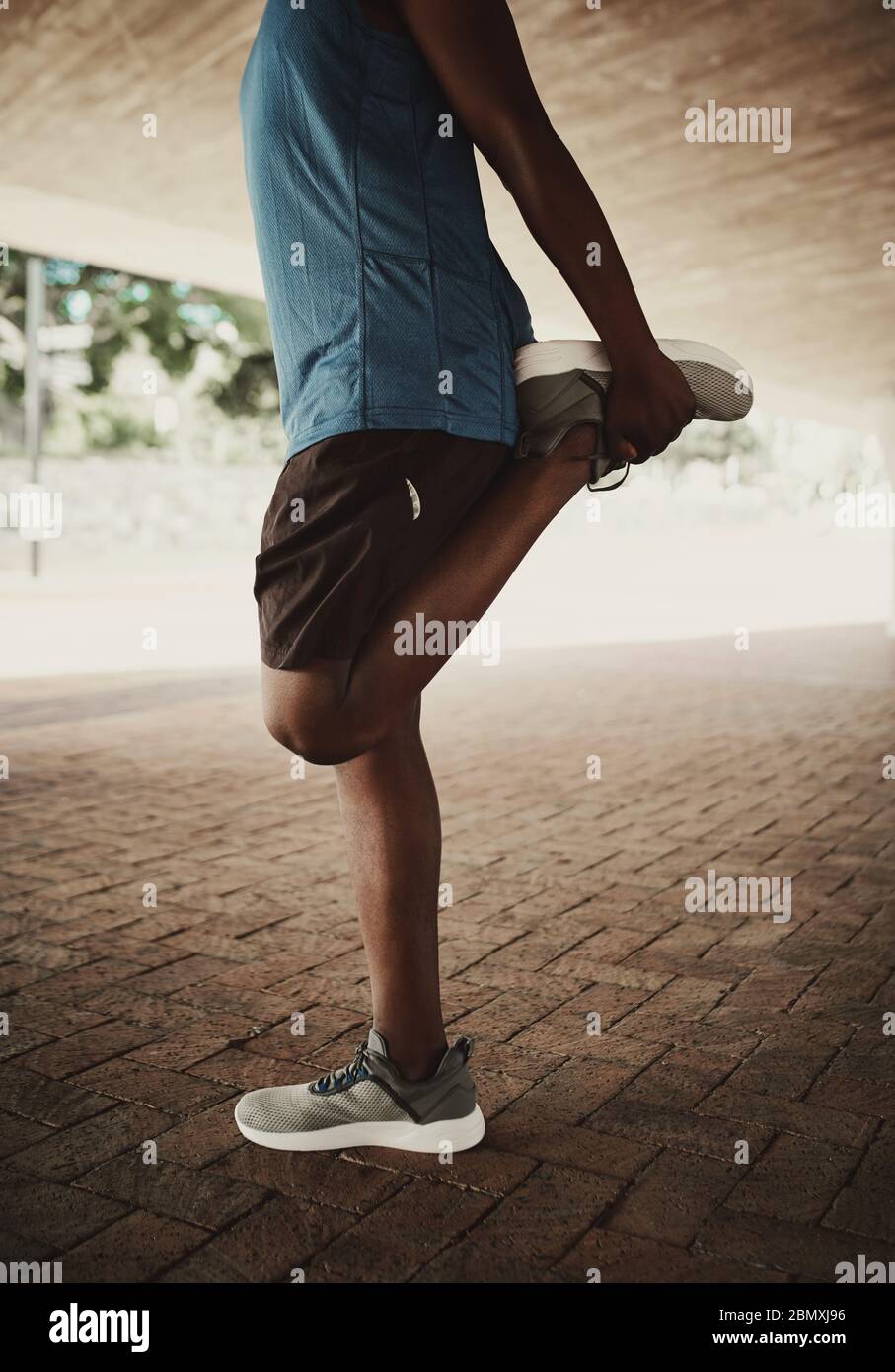 Sezione bassa di un uomo afroamericano sano di stile di vita che allunga le gambe prima di correre sulla strada della città Foto Stock