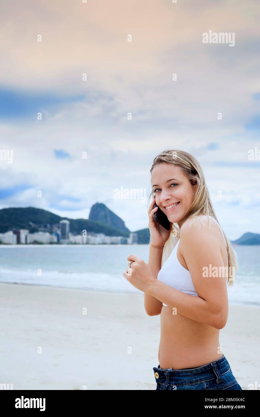 Una giovane turista femminile in un bikini utilizzando il suo cellulare sulla spiaggia in Sud America Foto Stock