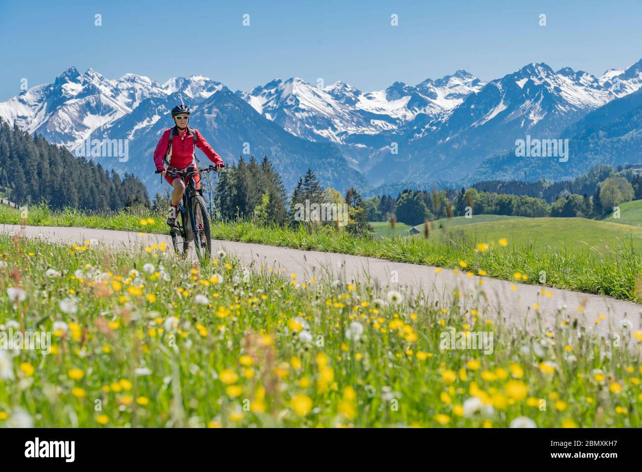 Bella donna anziana che cavalca la sua montagna elettrica in caldo giorno di primavera con snoe capped bike nella valle Iller vicino Oberstdorf con snoe capped Allgau Foto Stock