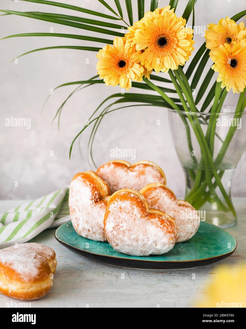 Un piatto con ciambelle a forma di cuore accanto ad un vaso con fiori gialli Foto Stock