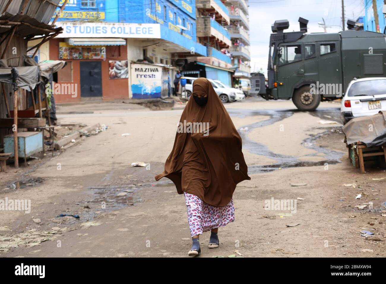 Una donna cammina davanti a un veicolo armato della polizia a Eastleigh durante la protesta.i residenti di Eastleigh hanno preso alla strada per protestare la restrizione del movimento nella zona a causa del caso diffuso di Covid-19 all'interno della zona residenziale e ha fatto appello al governo per fornire loro cibo di soccorso. Il Kenya ha confermato 672 casi di Covid-19 e 32 morti. Foto Stock