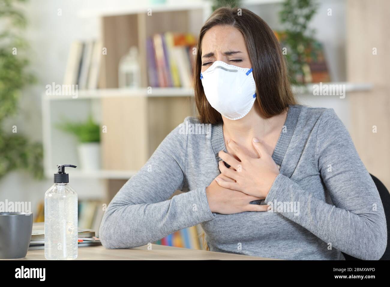 Donna malata di coronavirus con maschera protettiva soffocante che tiene il petto seduto a casa Foto Stock