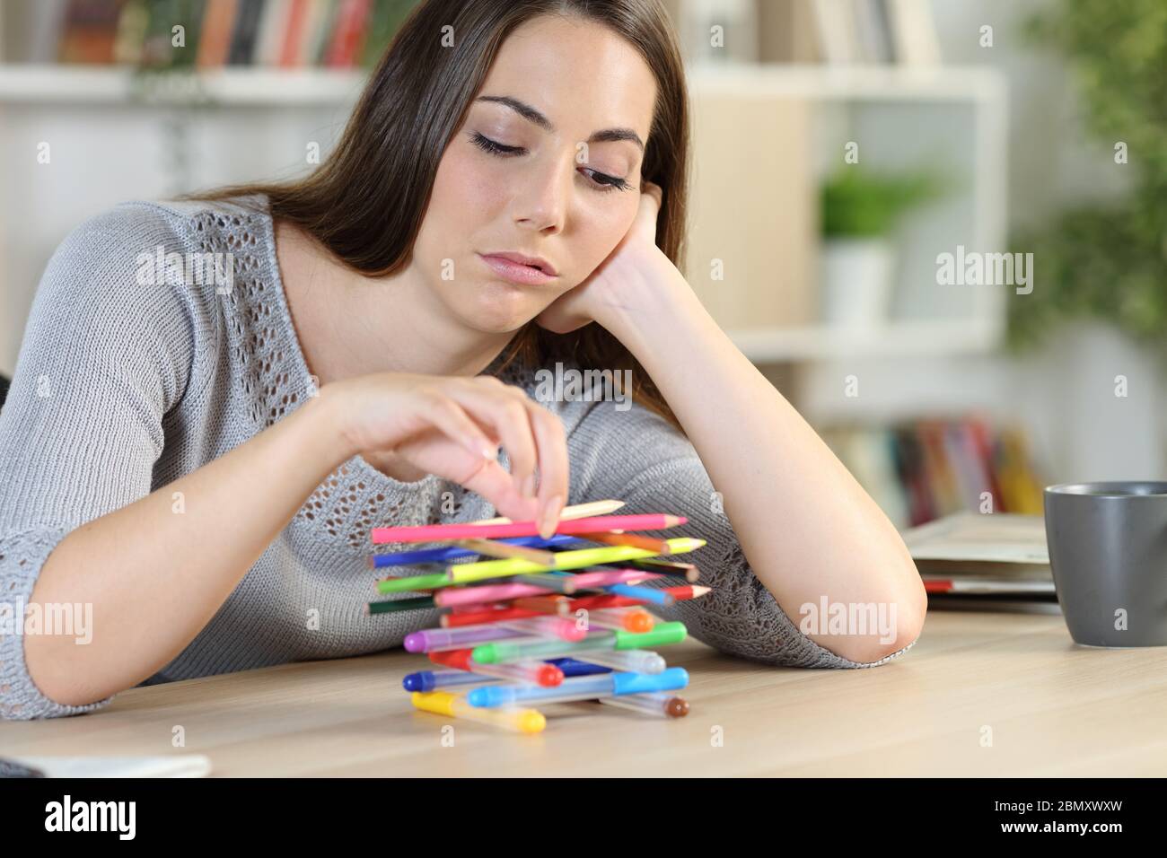 Donna pigra annoiata che spreca tempo giocando con matite sedute su una scrivania a casa Foto Stock