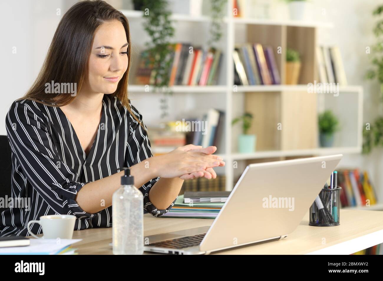 Donna imprenditore felice disinfettare le mani con gel igienizzante seduto su una scrivania a casa Foto Stock