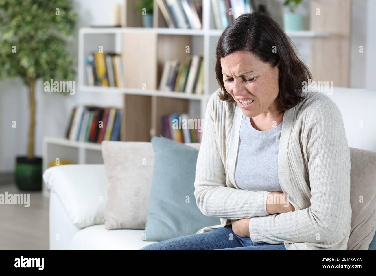 Donna di mezza età in dolore che soffre un mal di stomaco che tiene il pancia seduta sul divano a casa Foto Stock