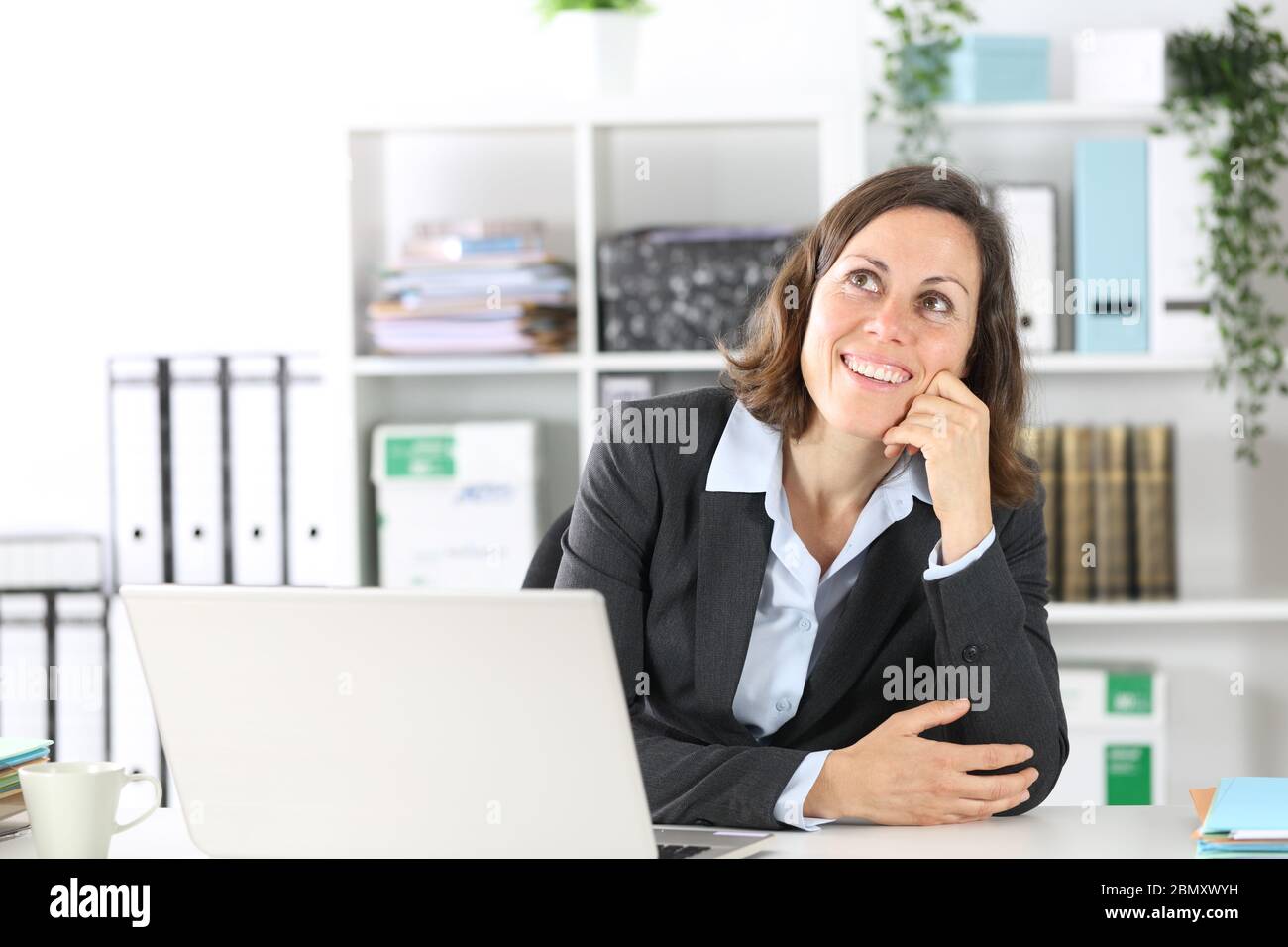 Una donna esecutiva pensante che guarda in alto mentre si siede su una scrivania in ufficio Foto Stock