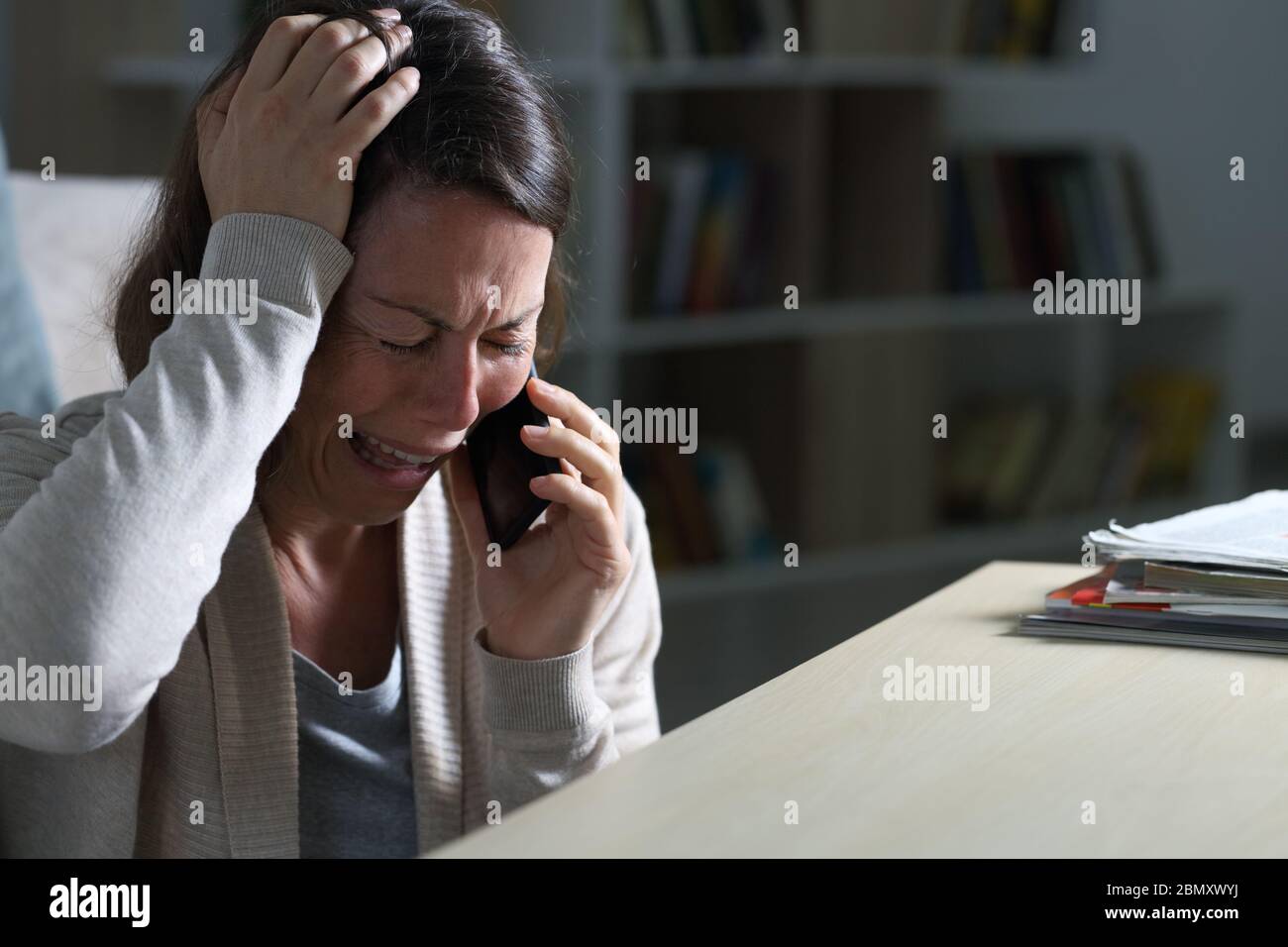 Triste donna di mezza età che piange chiamando su smartphone seduto sul pavimento di notte a casa Foto Stock