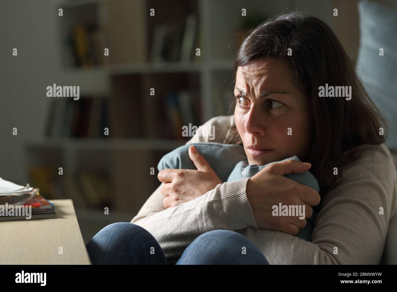 Donna di mezza età spaventata che guarda via seduta sul pavimento che tiene il cuscino di notte a casa Foto Stock