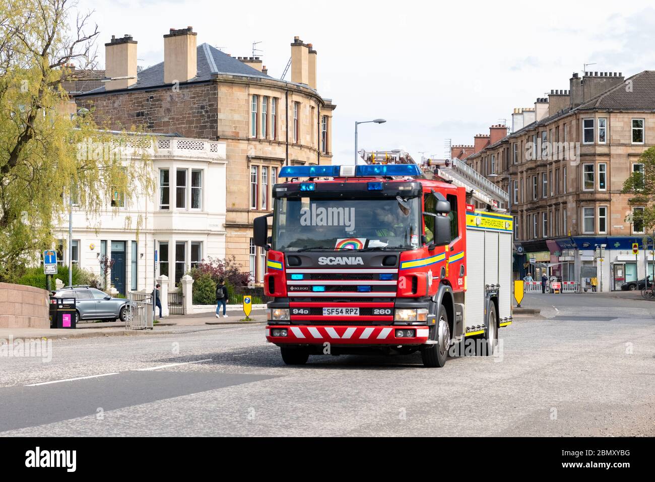 Motore antincendio con luci blu che rispondono a un'emergenza durante il blocco dei coronavirus, Glasgow, Scozia, Regno Unito - con immagine dell'arcobaleno sul parabrezza Foto Stock