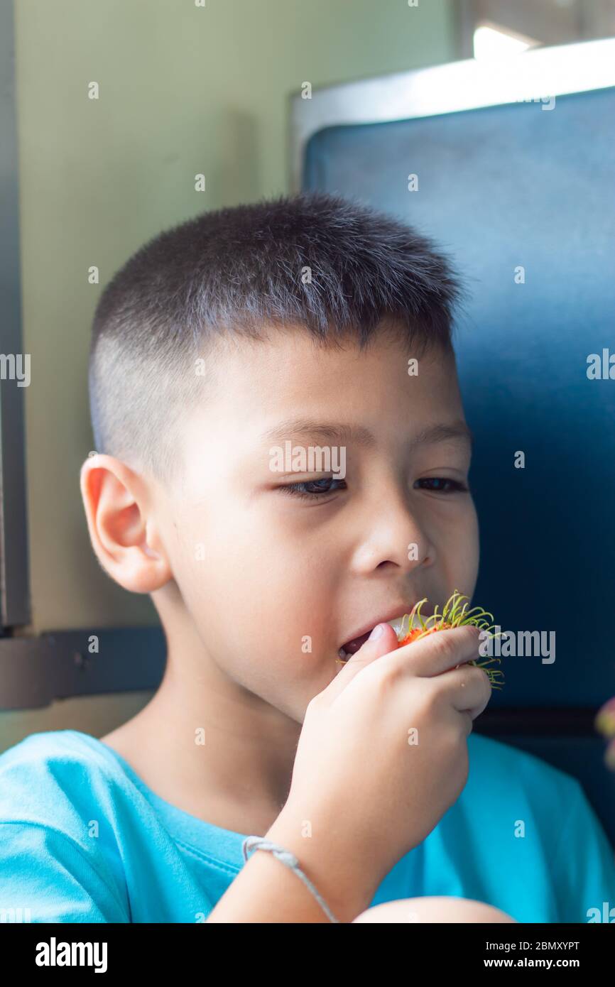 Immagini come un ragazzo seduto a mangiare Rambutan. Foto Stock