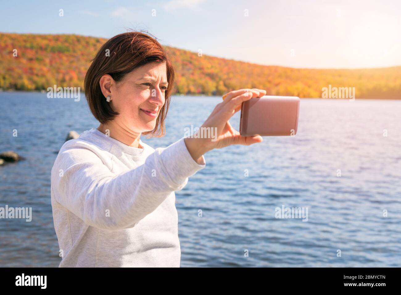 Donna che prende un selfie su un lago di montagna in una giornata di autunno soleggiato. Splendidi colori autunnali sullo sfondo. Foto Stock