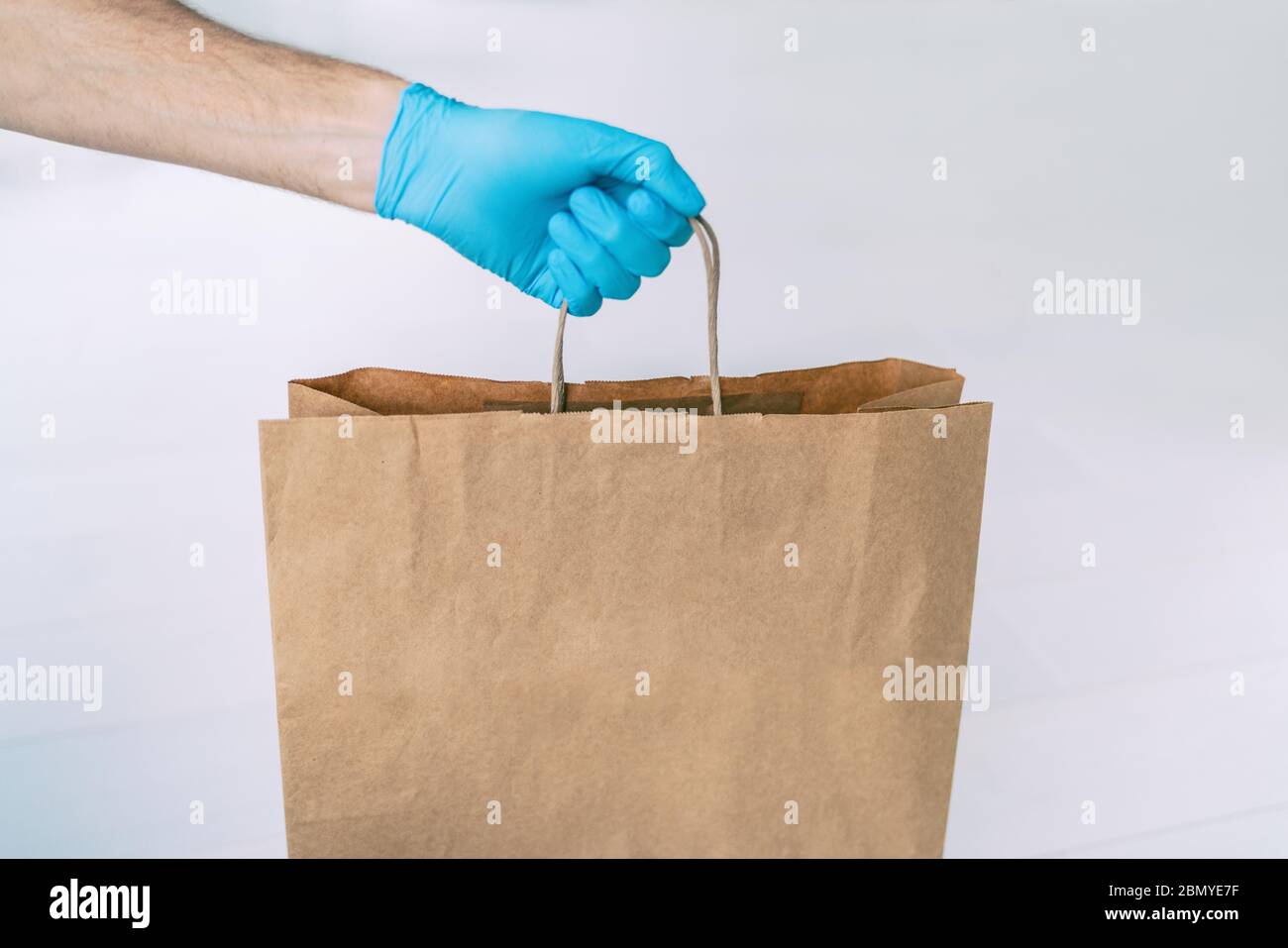 Consegna a domicilio durante la quarantena COVID-19 da coronavirus autoisolamento blocco. Uomo di consegna di shopping del negozio di alimentari che dà sacchetto di carta che indossa blu Foto Stock