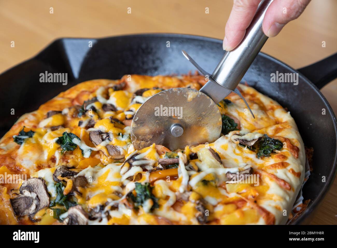 Taglierina per pizza affettare pizza vegetariana fatta in casa con funghi, spinaci; cipolla; formaggio; peperone; e varietà di condimenti vegetali e h aromatico Foto Stock