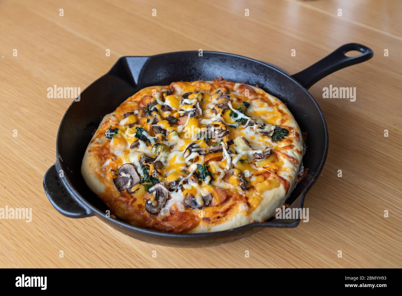 Pizza in padella vegetariana fatta in casa con funghi, spinaci, cipolla, formaggio, peperone e varietà di condimenti vegetali ed erbe aromatiche Foto Stock