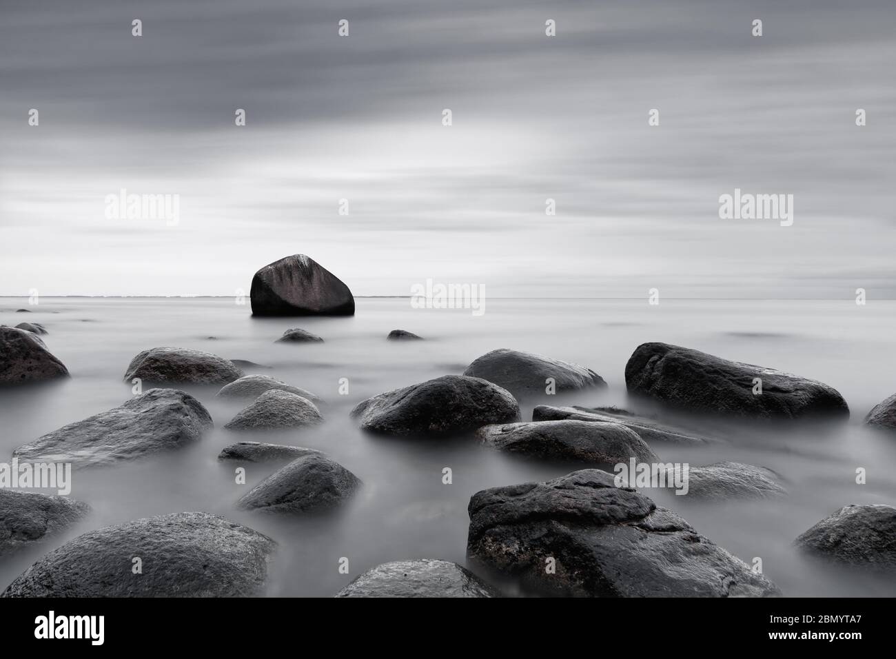 Immagine in bianco e nero con grandi pietre sulla spiaggia del Mar Baltico, il movimento dell'acqua e delle nuvole è stato levigato da esposizione a lungo tempo, l'immagine radi Foto Stock