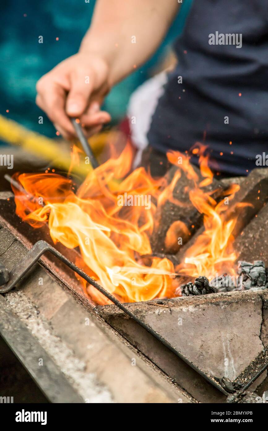 Puyallup, Washington, Stati Uniti. Fabbro femmina che riscalda un ferro nella fiamma di una fucina portatile. Foto Stock