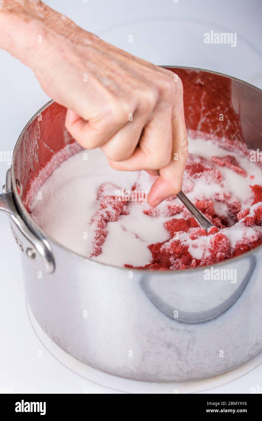 Donna che mescola lo zucchero in una pentola di lamponi schiacciati in marmellata-fare. Lo zucchero estrae l'acqua dalla frutta e forma legami chimici che "legano" il Foto Stock