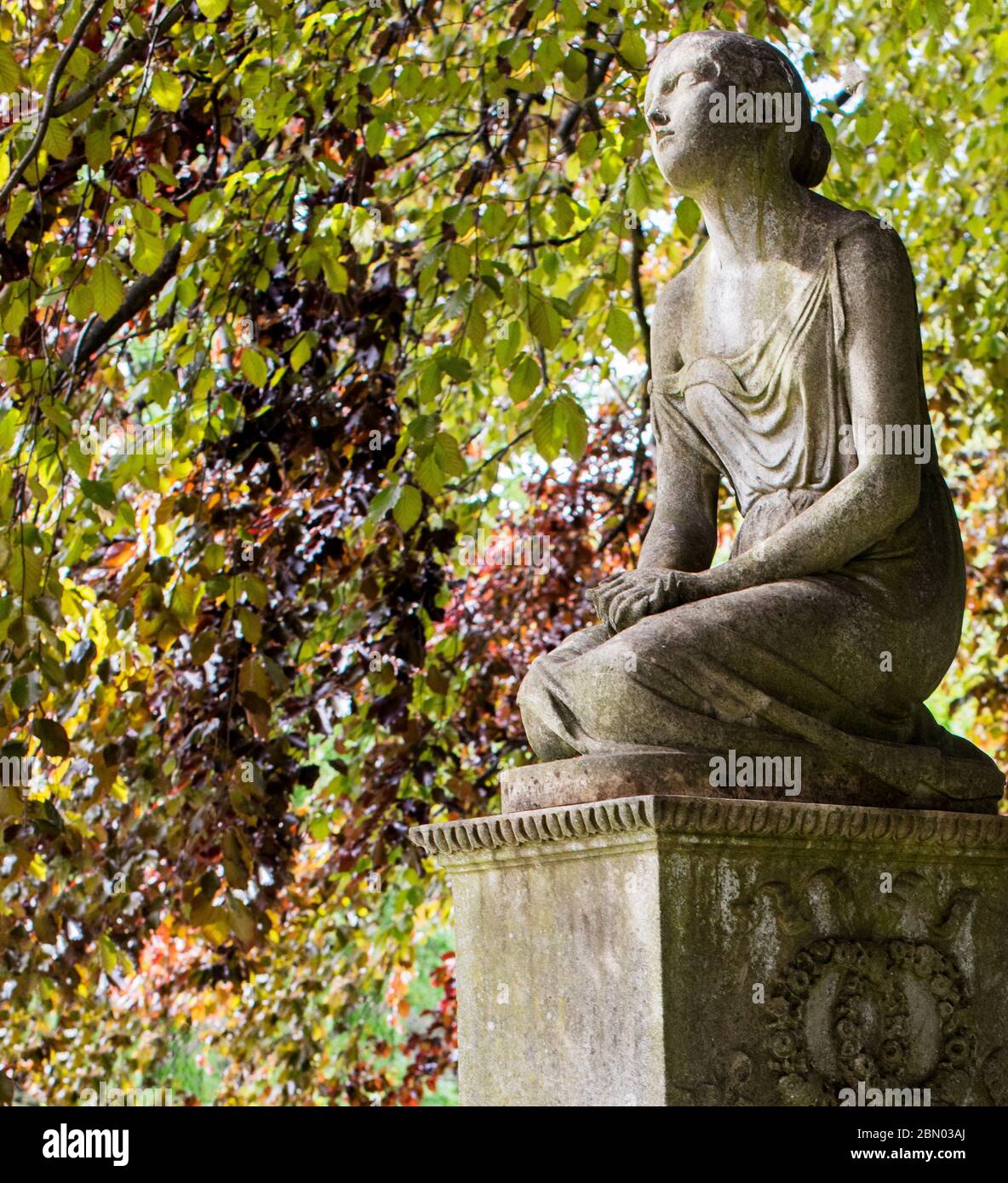 Statua di giovane ragazza sulla lapide con uno schermo di foglie di rame faggio nel Cimitero di Brompton, Kensington, Londra. Foto Stock