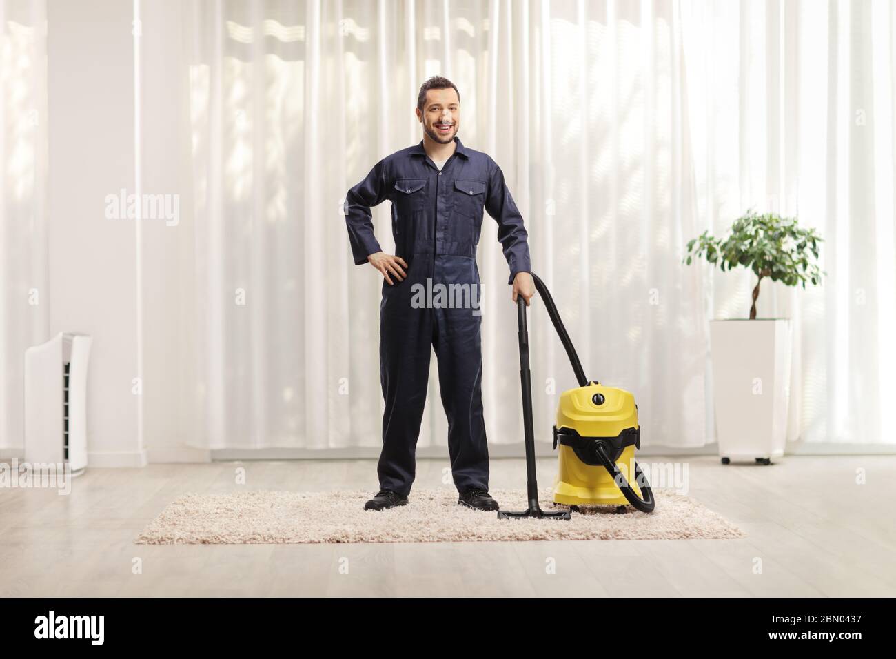 Ritratto a tutta lunghezza di un lavoratore maschile in uniforme con un aspirapolvere in casa Foto Stock