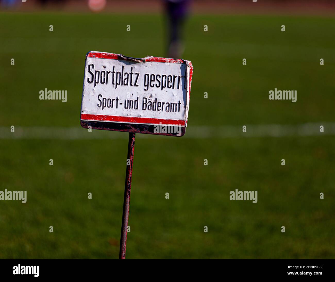 Un cartello di metallo consumato con la scritta "Campo sportivo chiuso, Ufficio sport e bagni" si trova su un'asta nell'erba di un campo sportivo in Gladbacher Straße a Krefeld, Germania, con una persona visibile sfocata sul campo sullo sfondo Foto Stock