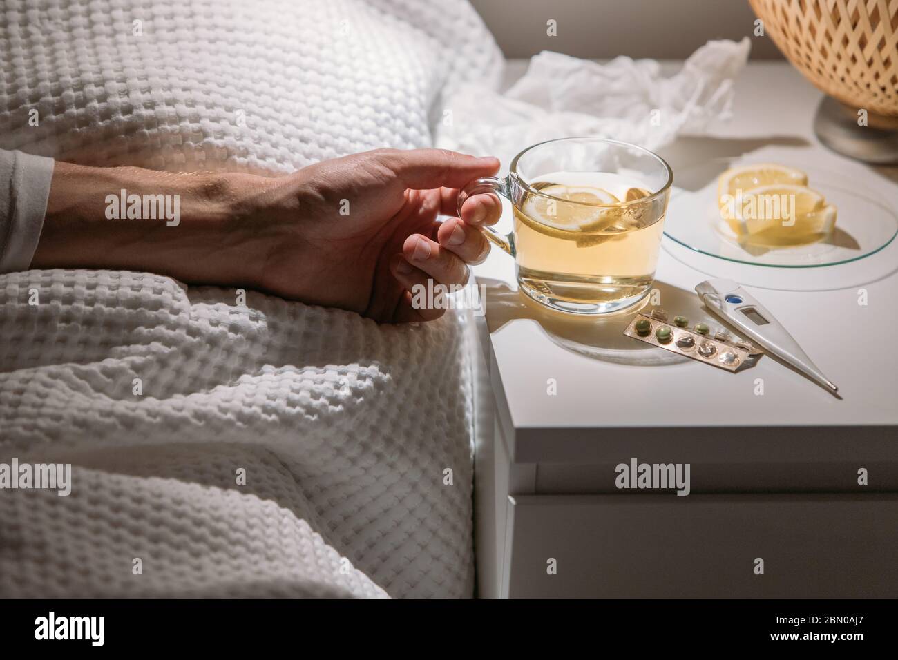 Uomo malato che si posa a letto sotto coperta e tenendo una tazza di tè caldo con limone, primo piano. Maschio bere bevande calde per ottenere bene da influenza, febbre e virus Foto Stock