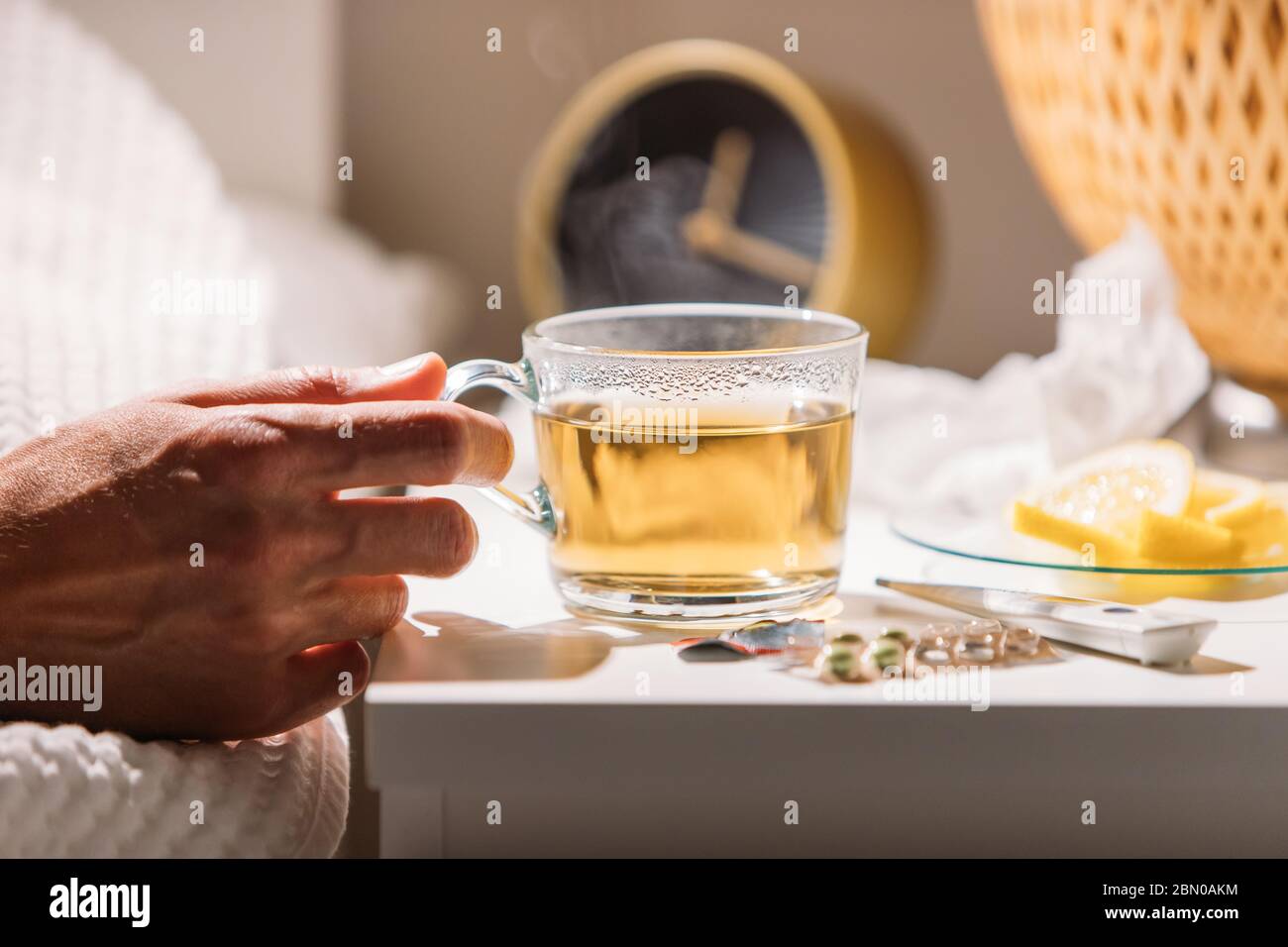 Uomo malato che si posa a letto sotto coperta e tenendo una tazza di tè caldo con limone, primo piano. Maschio bere bevande calde per ottenere bene da influenza, febbre e virus Foto Stock
