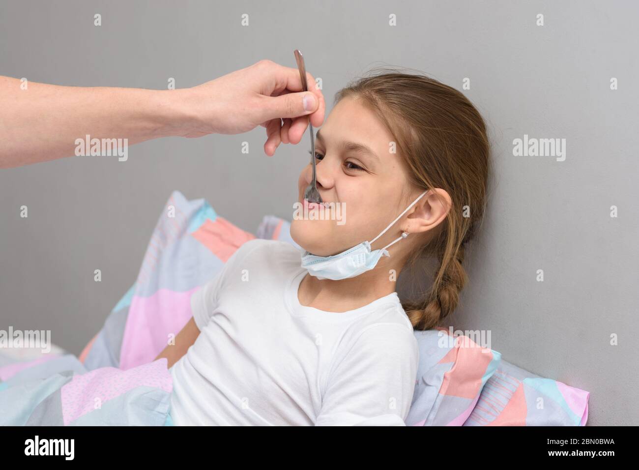 Una ragazza malata viene data medicina da un cucchiaio in bocca Foto Stock