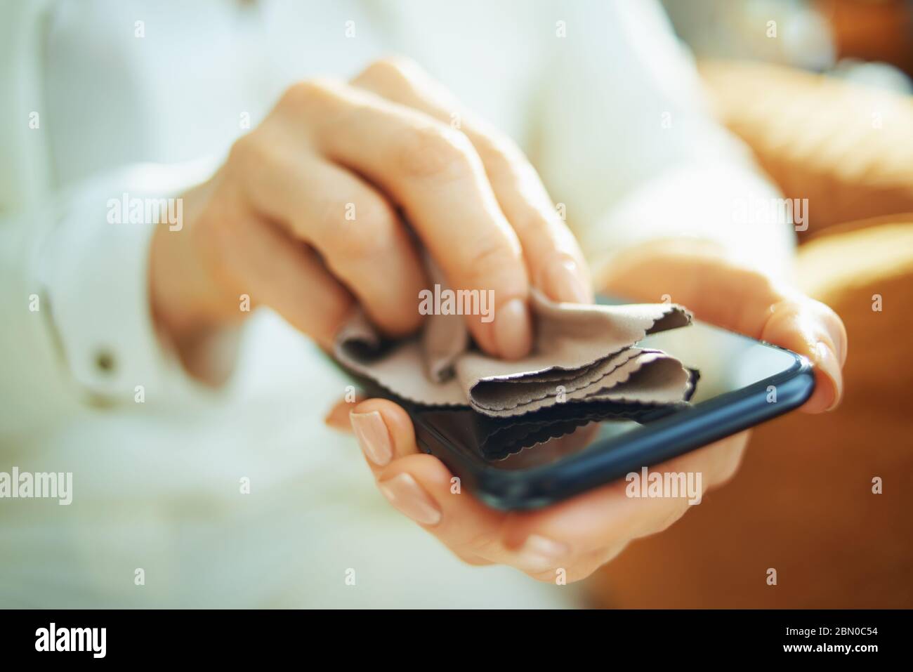 Primo piano su donna smartphone con panno per pulizia in casa durante il giorno di sole. Foto Stock