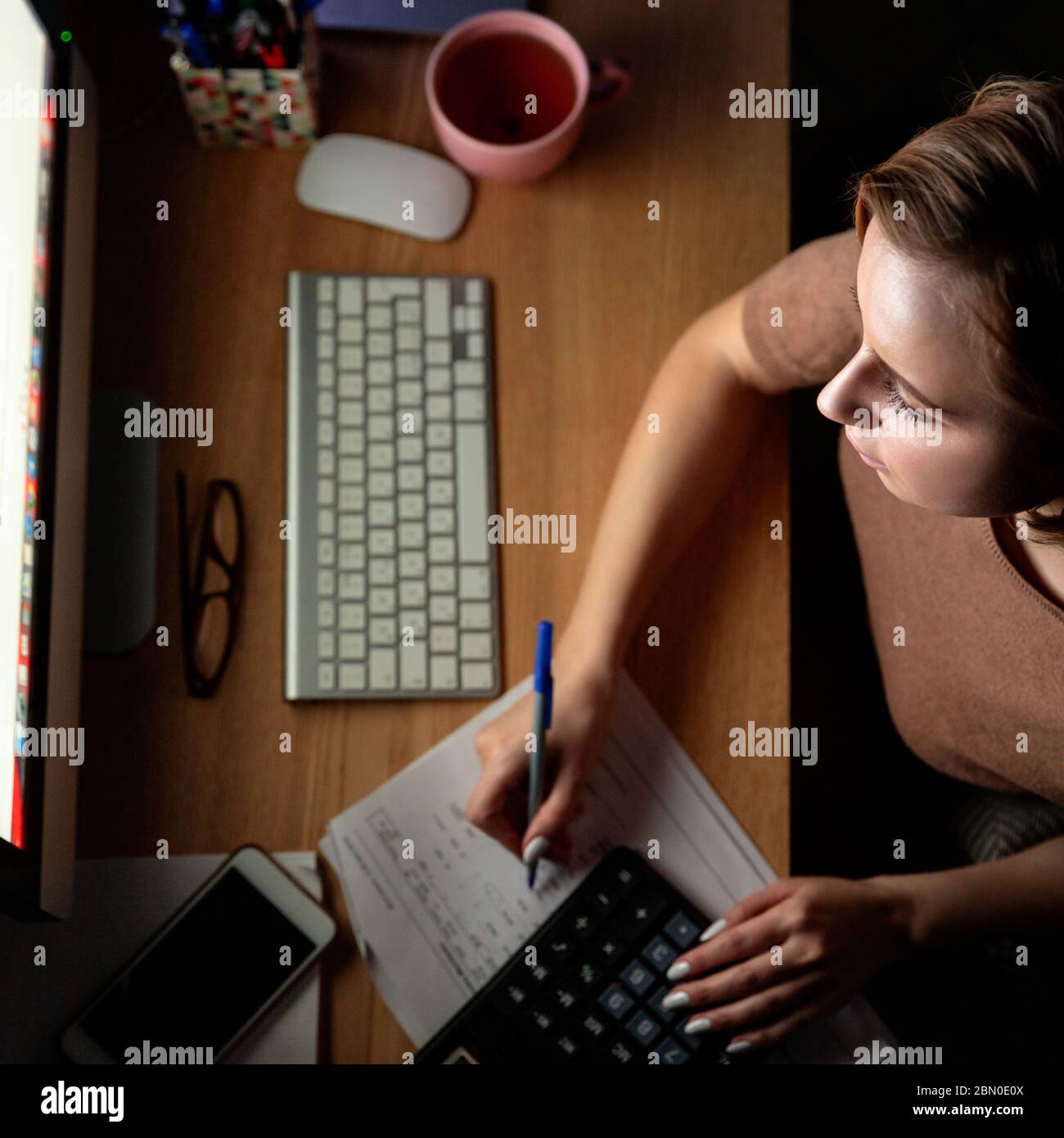 Donna che usa la calcolatrice per calcolare la fattura, pianificare le spese, tenere una penna, lavorare su PC desktop a tarda notte in ufficio, non può dormire.F. Foto Stock