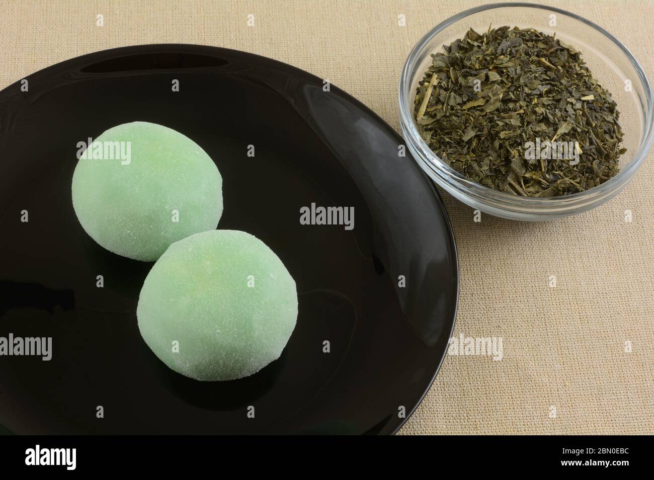 Tè verde gelato palline mochi su piatto nero dessert con tè verde in una ciotola di vetro su tovaglia marrone Foto Stock
