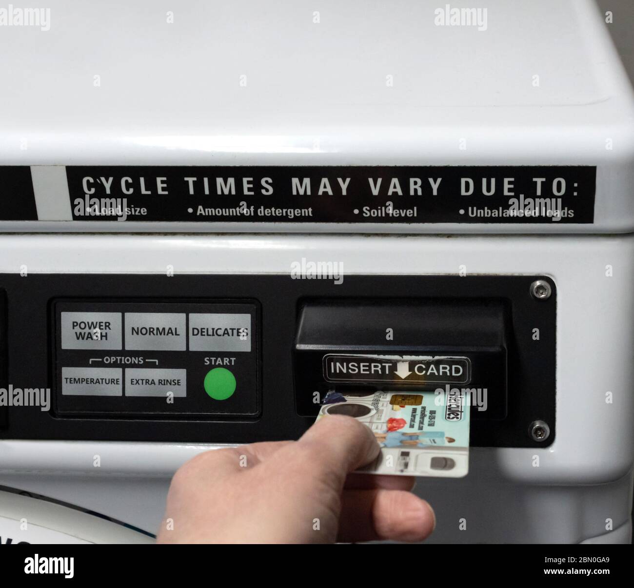 Mano che inserisce la carta di pagamento di marca di Hercules in una lavatrice basata tassa. Pulsanti per le impostazioni del ciclo visibili. Foto Stock