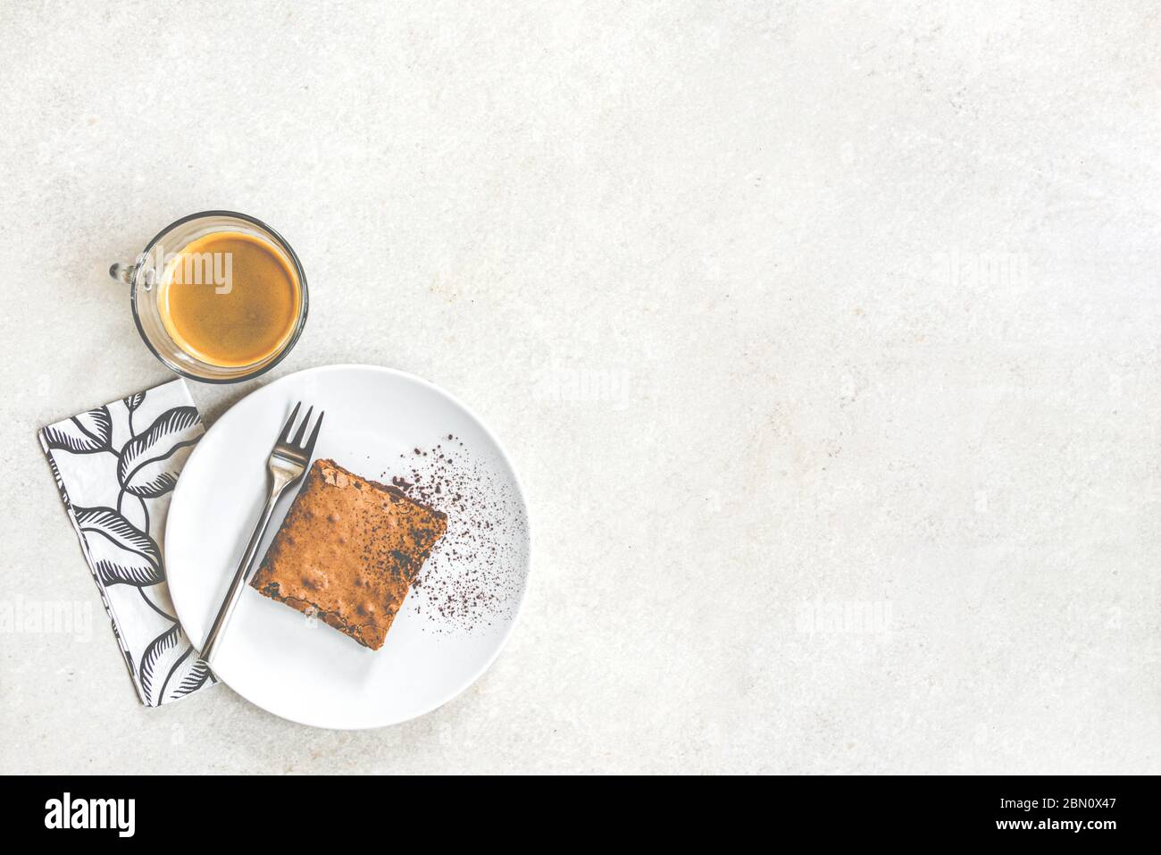 Vista dall'alto di una tazza di caffè e un piatto da dessert con torta di brownie su sfondo rustico bianco. Foto Stock