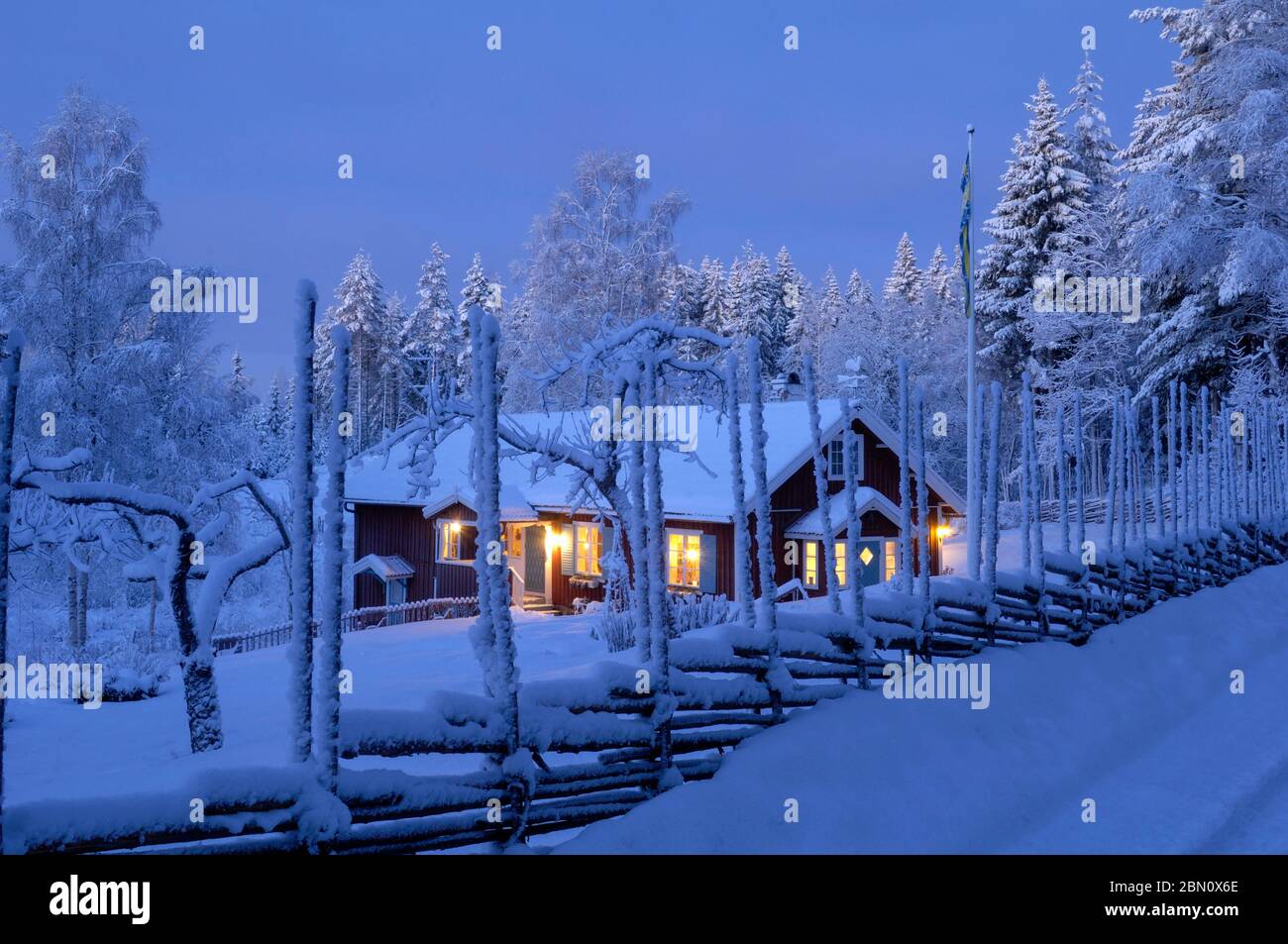 Una recinzione coperta di neve di fronte a una tradizionale casa rossa falu, Boda Kyrkby, Rättvik, Dalarna Foto Stock