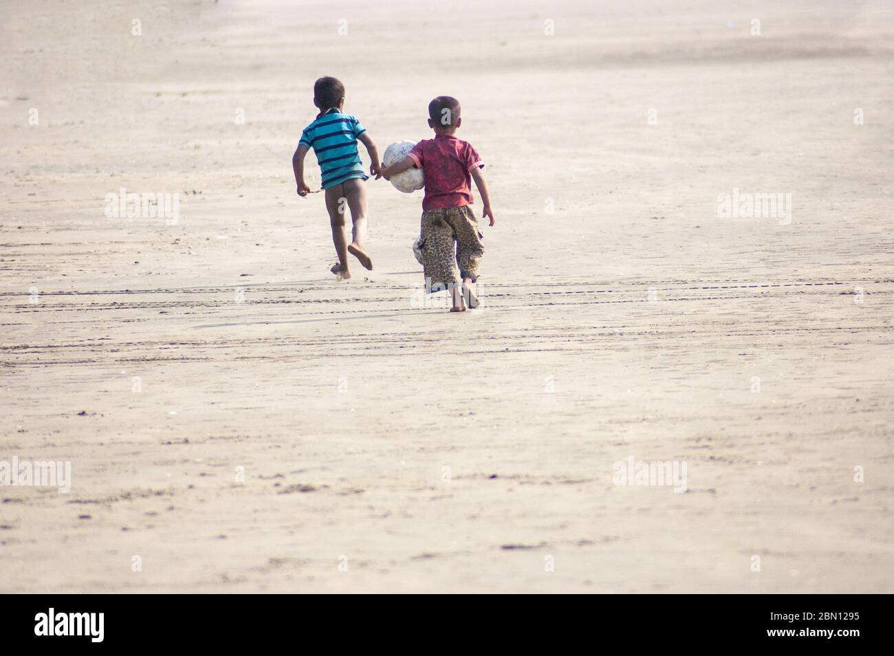 Due ragazzi che corrono gioiosamente con una palla su una spiaggia Foto Stock