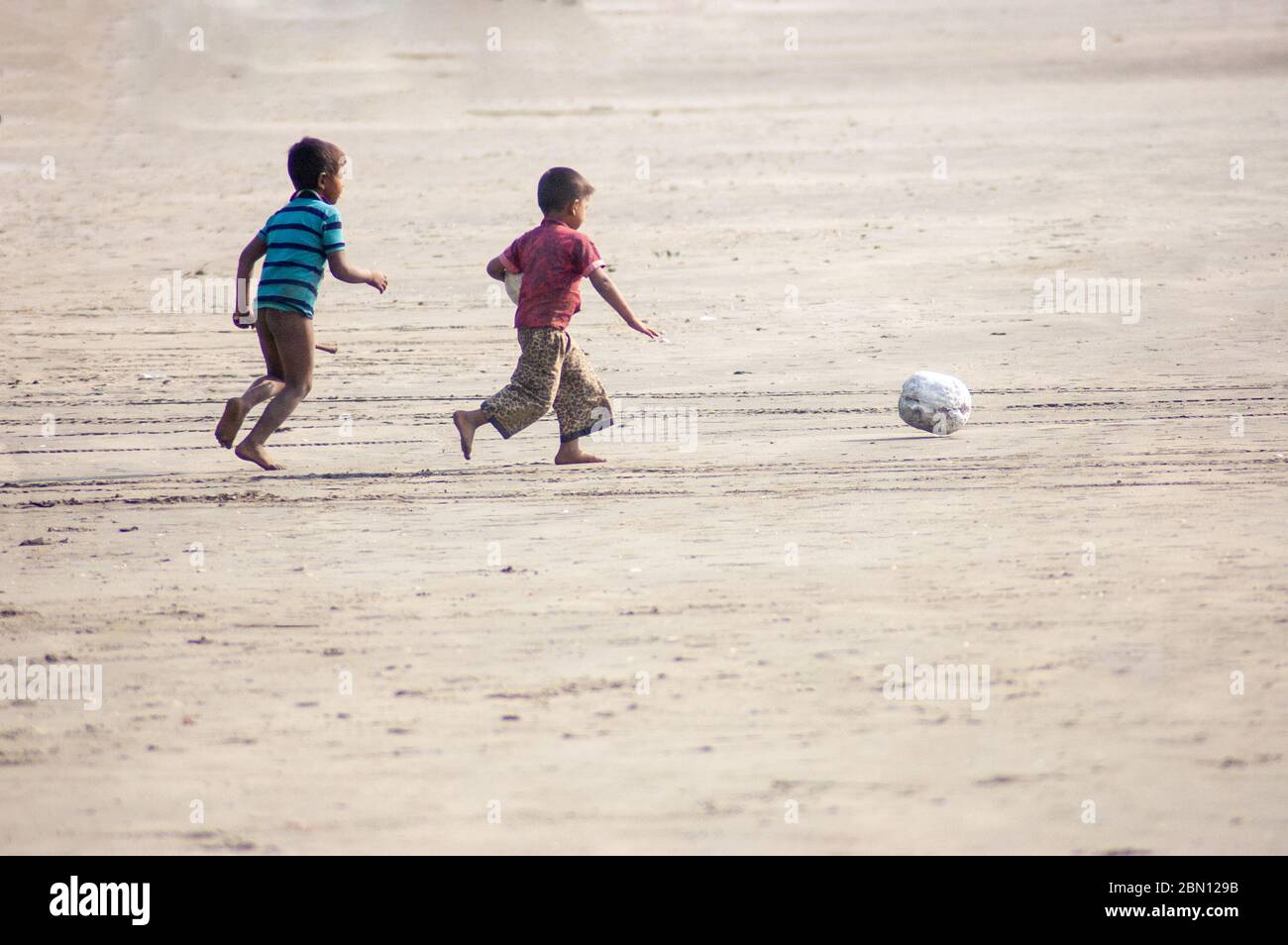 Due ragazzi che corrono gioiosamente con una palla su una spiaggia Foto Stock