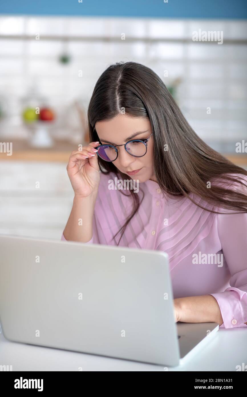 Donna in una blusa rosa che indossa occhiali guardando coinvolto Foto Stock