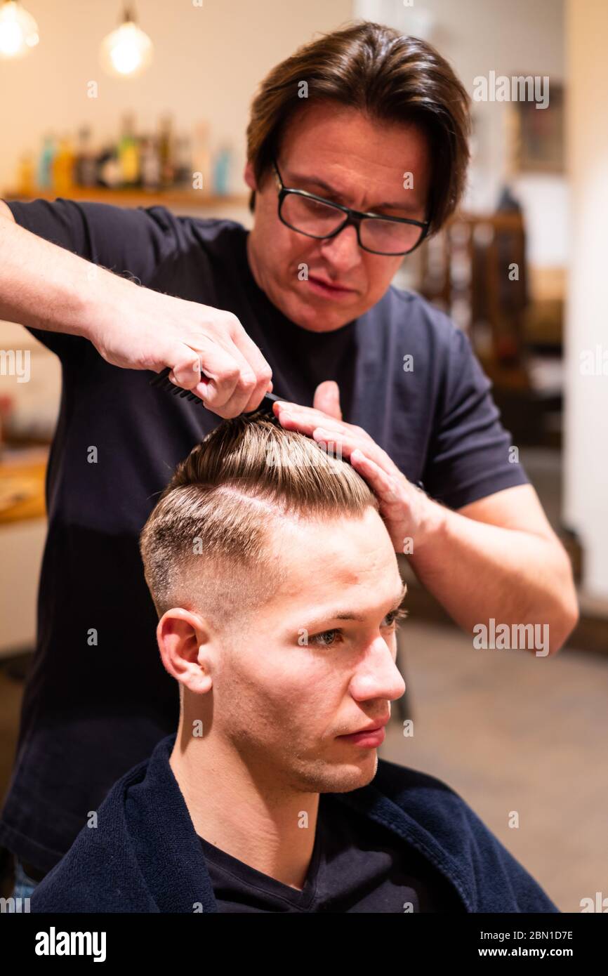 Barber pettina i capelli di un giovane dopo aver tagliato i capelli nel suo barbiere Foto Stock