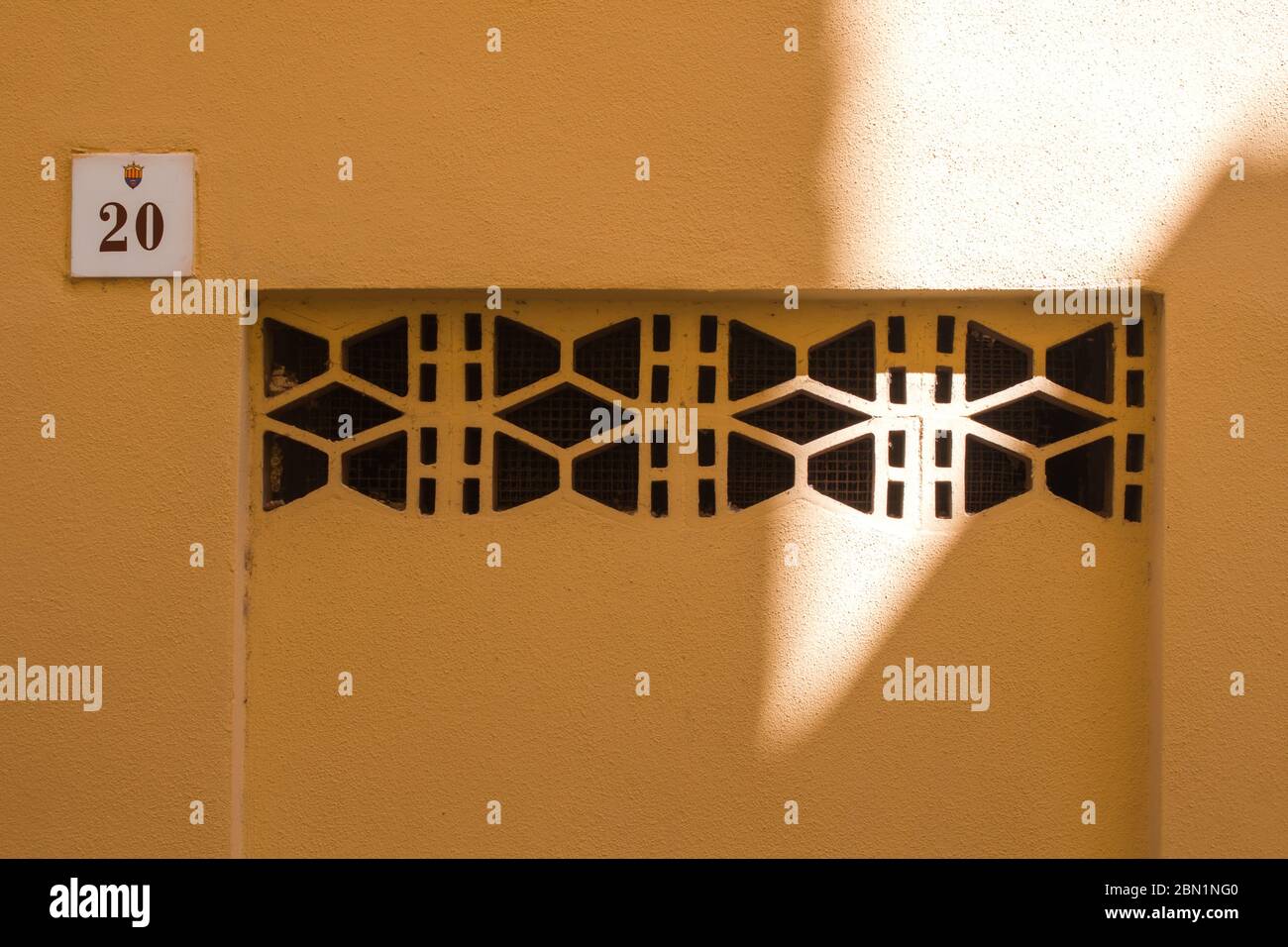 Facciata gialla di una casa con un elegante fori di ventilazione e con una piastra con numero venti. Contrasto di ombra e luce. Alghero, Sardegna, Ital Foto Stock