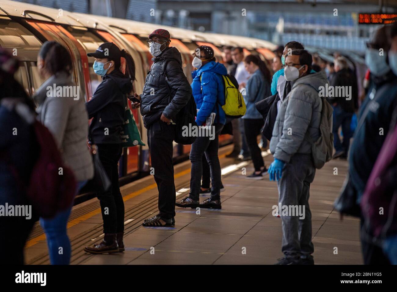 Passeggeri che indossano maschere facciali su una piattaforma alla stazione metropolitana di Canning Town a Londra. Foto Stock