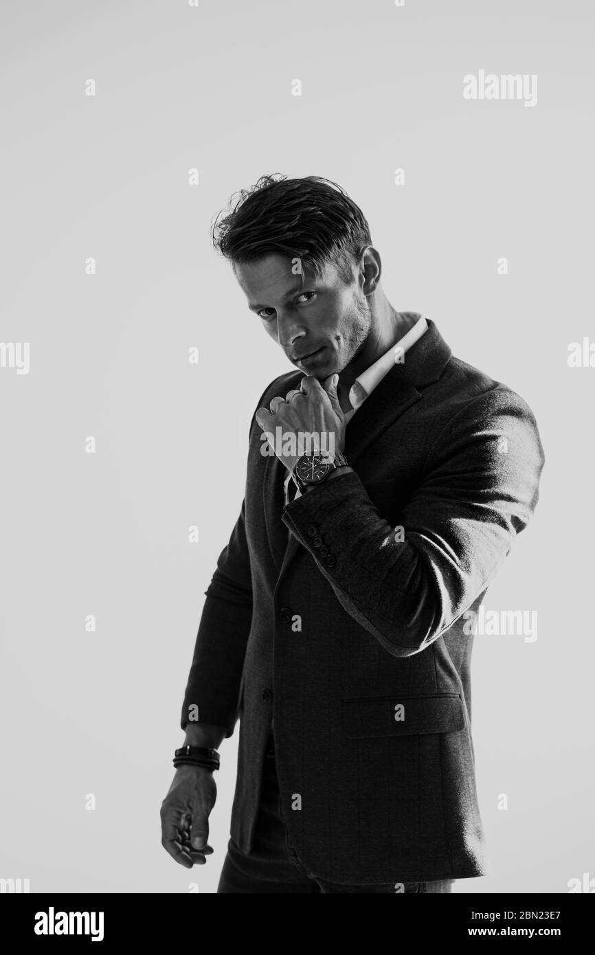 Ritratto di bell'uomo elegante in giacca e guardare su sfondo bianco. Ritratto dell'uomo di moda in interni. Foto in bianco e nero. Foto Stock
