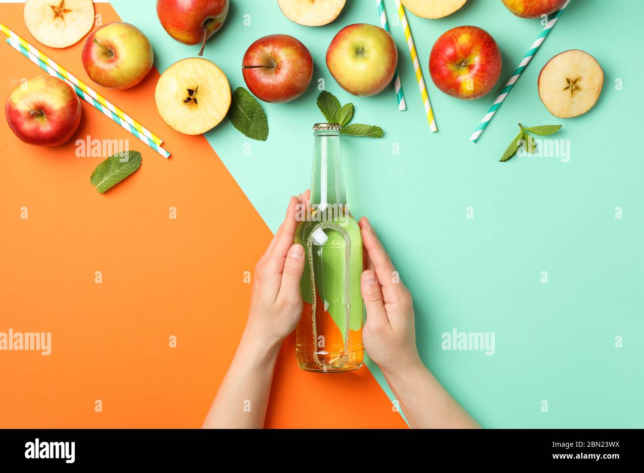 Le mani femminili tengono il flacone di sidro su sfondo a due toni. Composizione con sidro Foto Stock