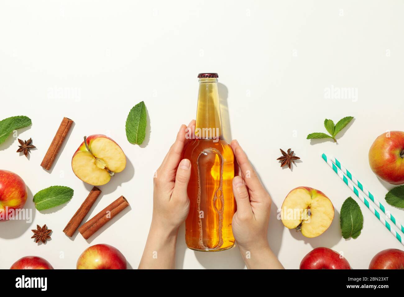 Le mani femminili tengono il flacone di sidro su sfondo bianco. Composizione con sidro Foto Stock