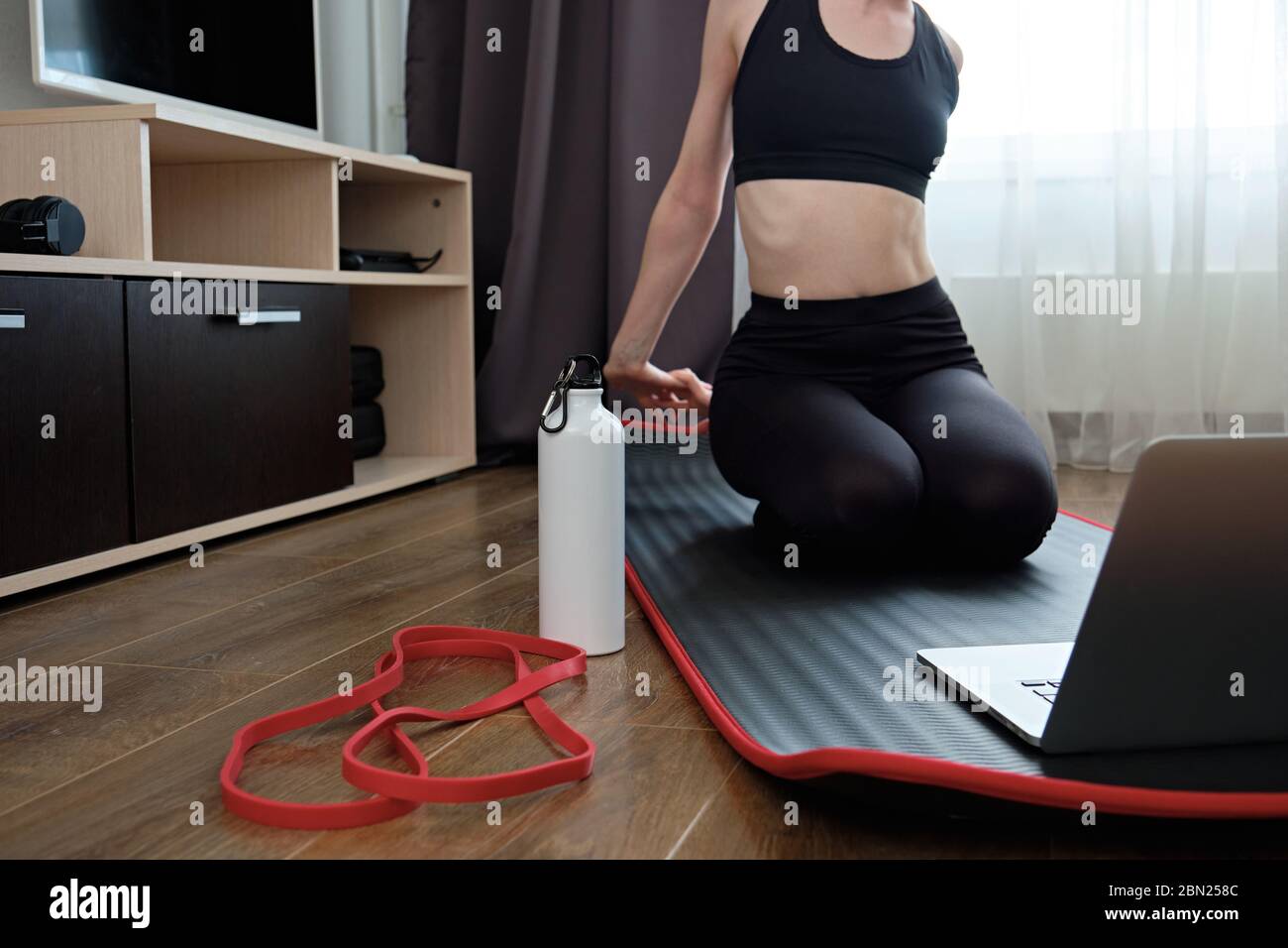 La ragazza è impegnata nello stretching di fronte al portatile, la bottiglia di sport fuoco vicino. Foto Stock