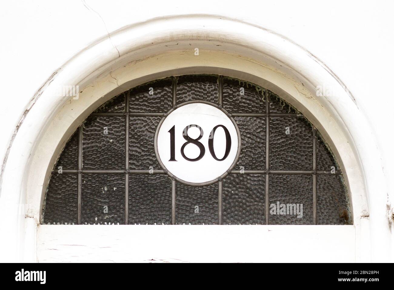 Casa numero 180 su una placca rotonda bianca in un semicerchio di vetro Foto Stock