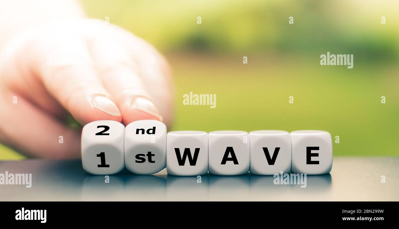 Simbolo di una seconda onda del virus corona. La mano gira i dadi e cambia l'espressione '1a onda' in '2a onda' Foto Stock