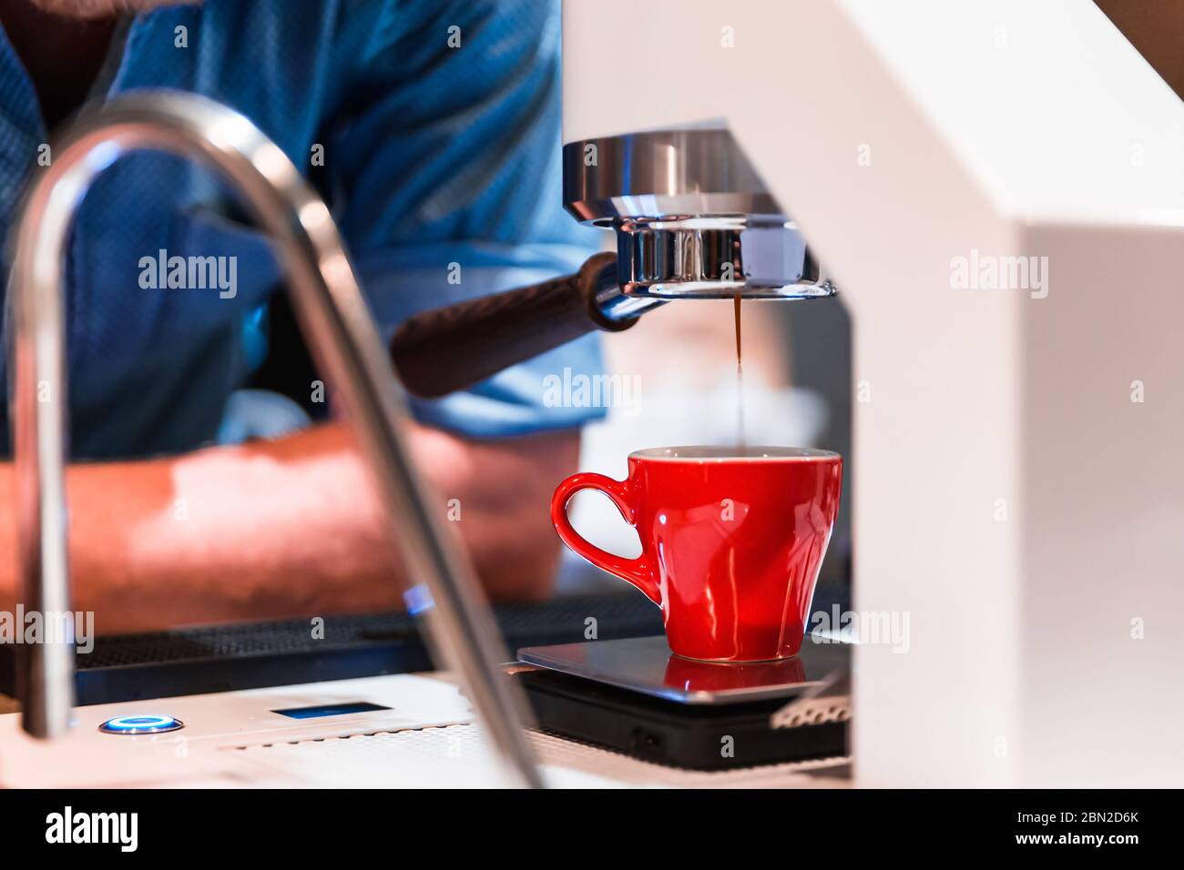 Barista in attesa di macchina per caffè per preparare un espresso che si versa nella piccola tazza rossa. Foto Stock