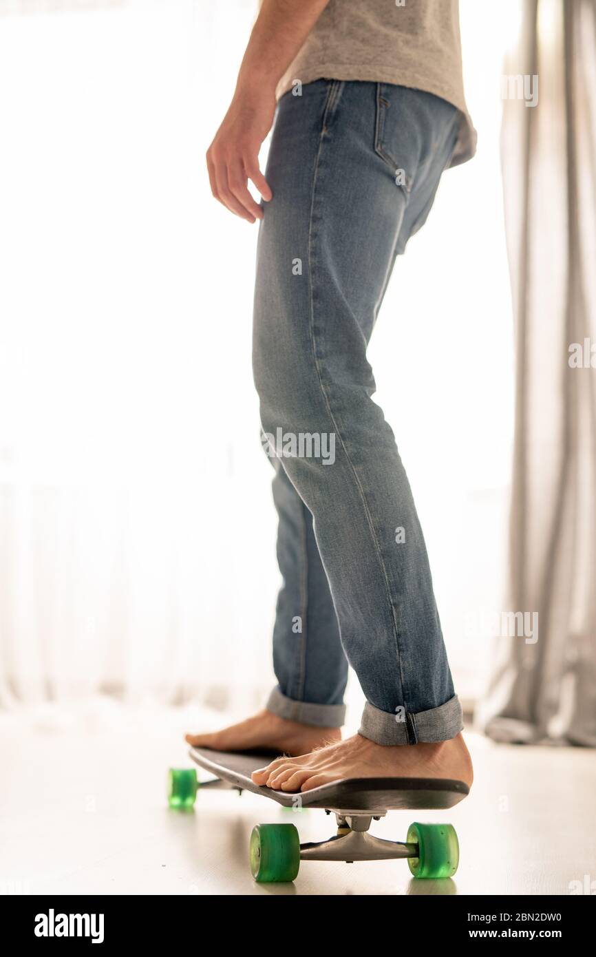Uomo irriconoscibile in jeans che imparano a skateboard sopra il soggiorno in casa isolamento Foto Stock
