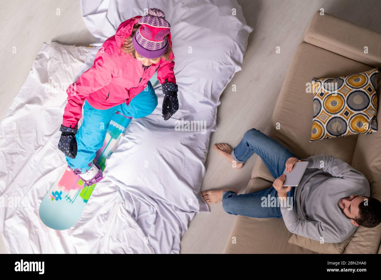 Sopra la vista del giovane uomo che legge consiglio su tablet alla ragazza che impara a snowboard in isolamento domestico Foto Stock