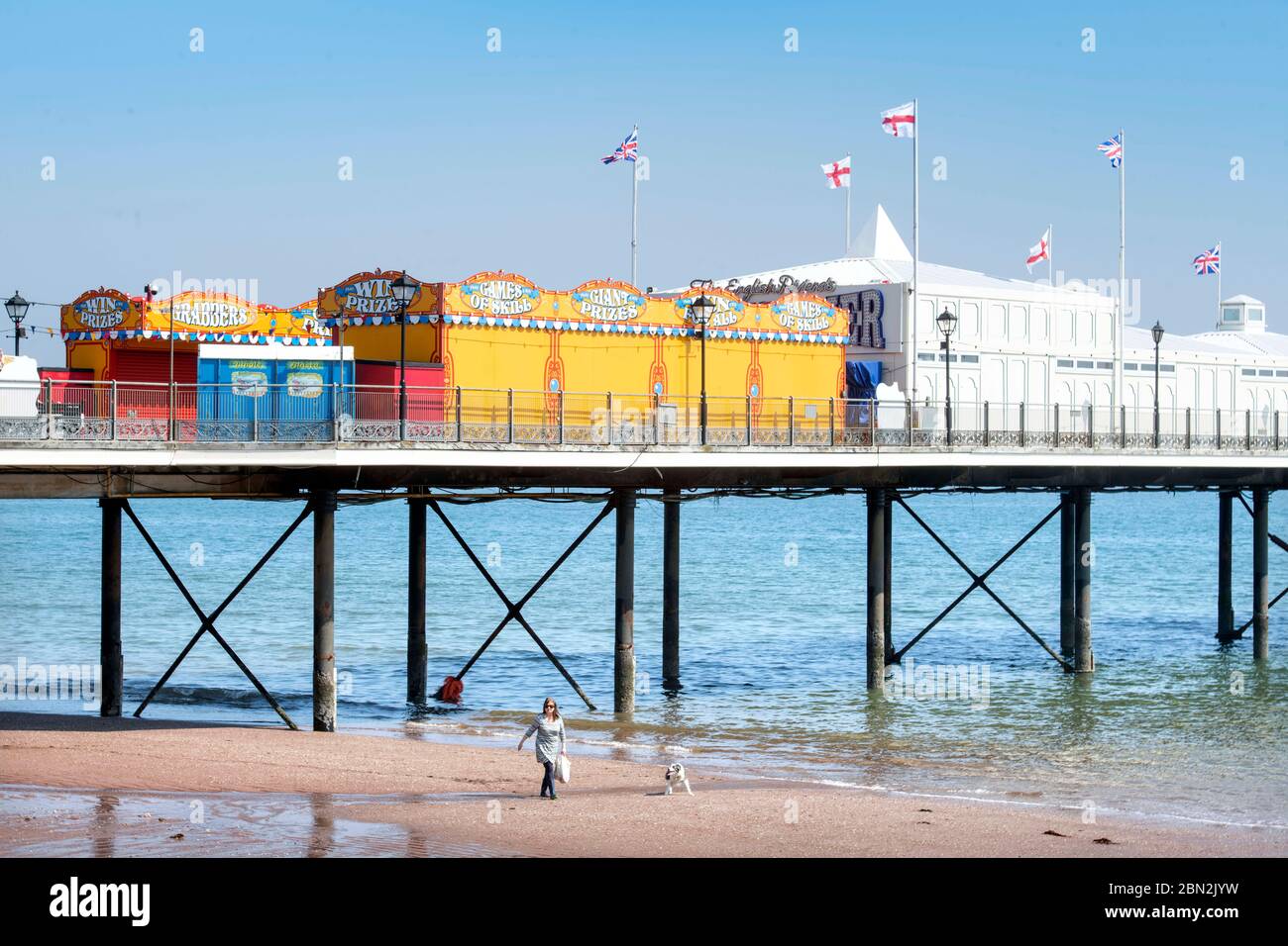 Una donna cammina il suo cane sotto il molo chiuso sulla spiaggia di Paignton durante il blocco di Coronavirus, Regno Unito Foto Stock