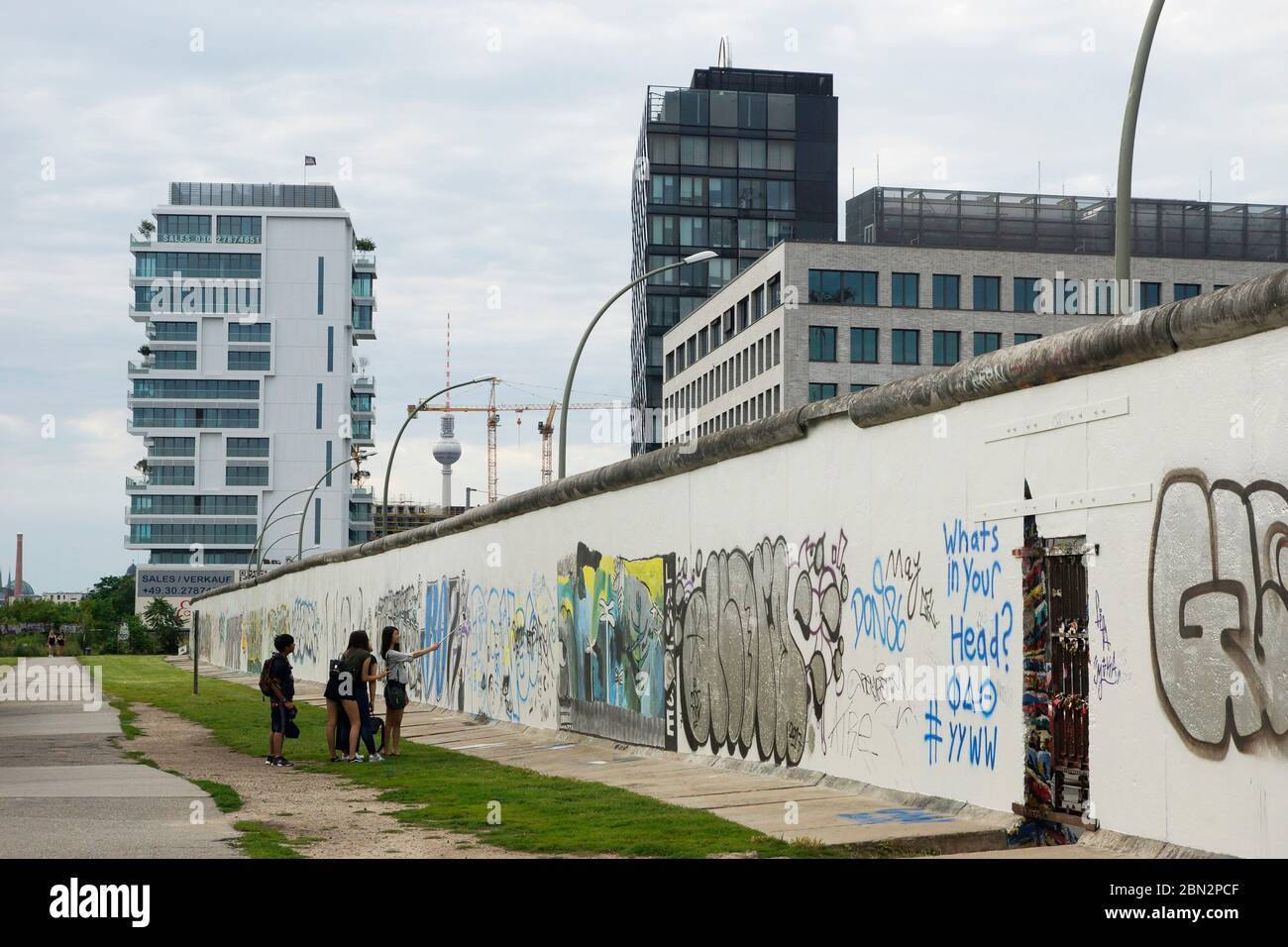 Ein Teil der Berliner Mauer (East Side Gallery) im Hintergrund neu erstellte Gebäude und der Fernsehturm Foto Stock